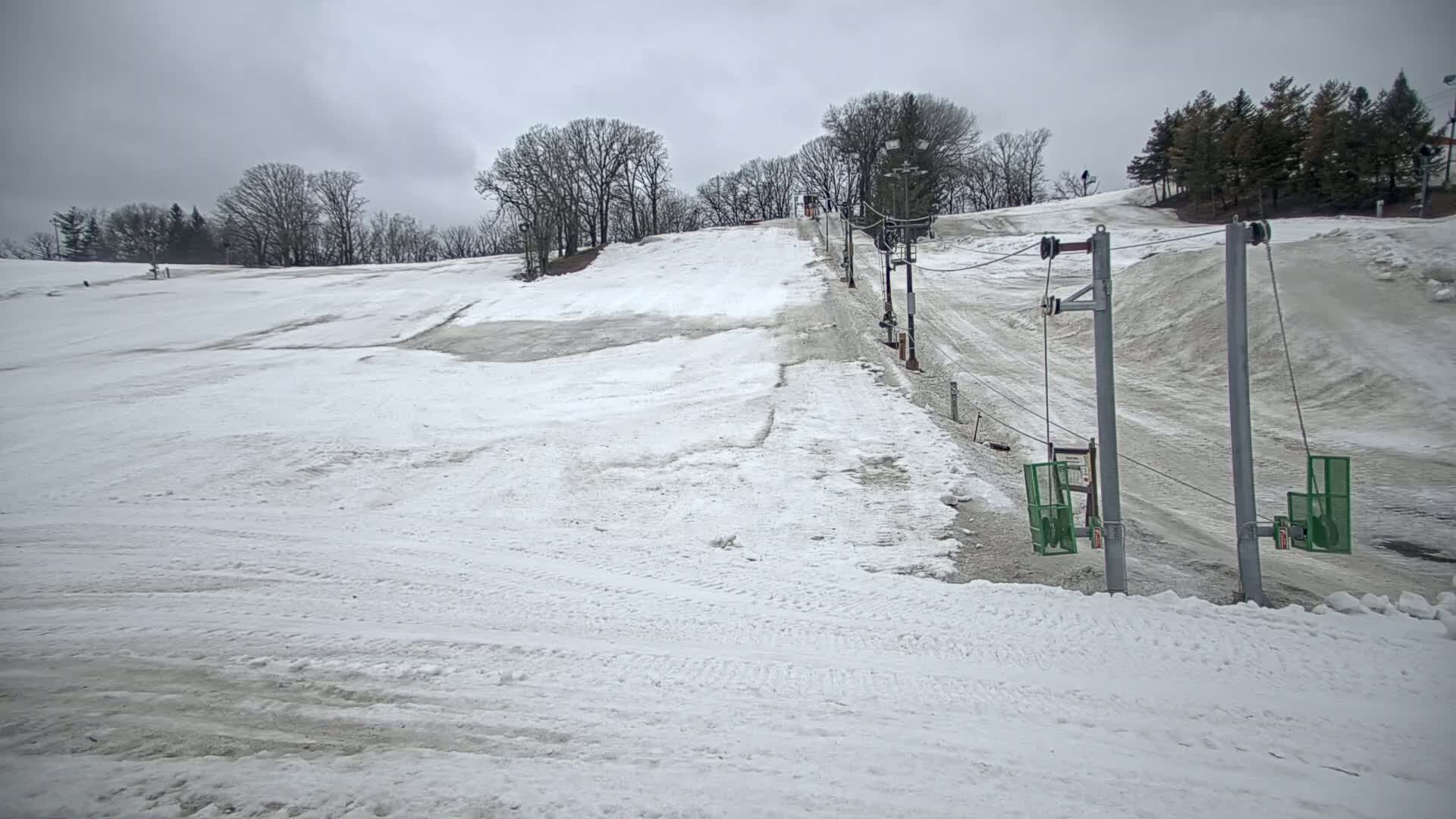 A snow-covered ski slope with a sparsely used surface lift under an overcast sky.