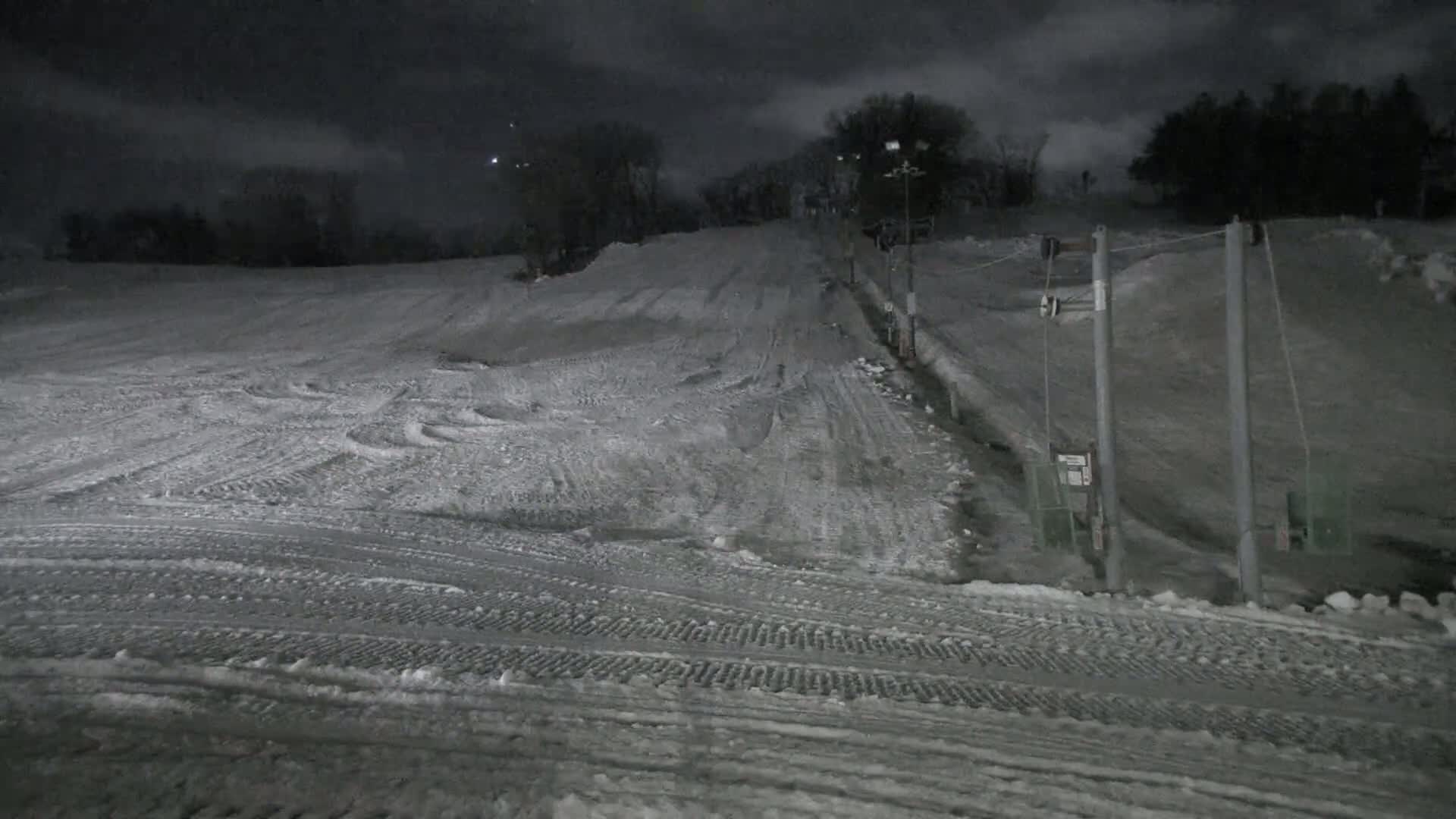A snow-covered ski slope at night, illuminated under a dark, cloudy sky.