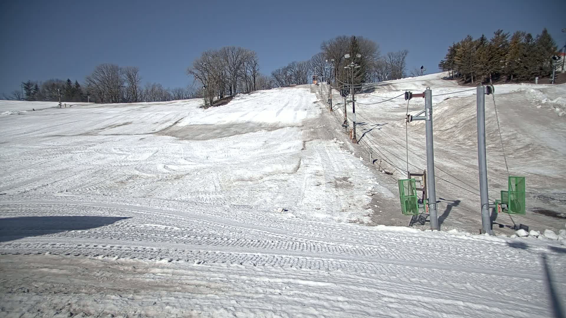 A snow-covered ski slope with a chairlift and leafless trees under a clear blue sky.