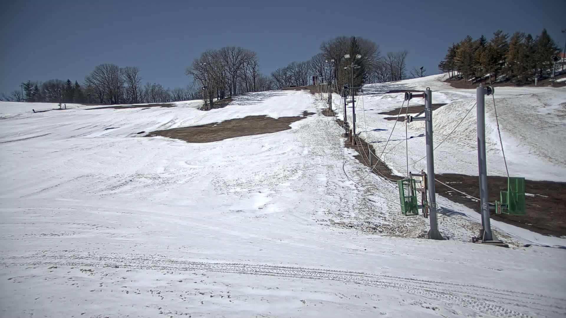 A snow-covered ski slope with a sparsely populated chairlift under a clear blue sky.