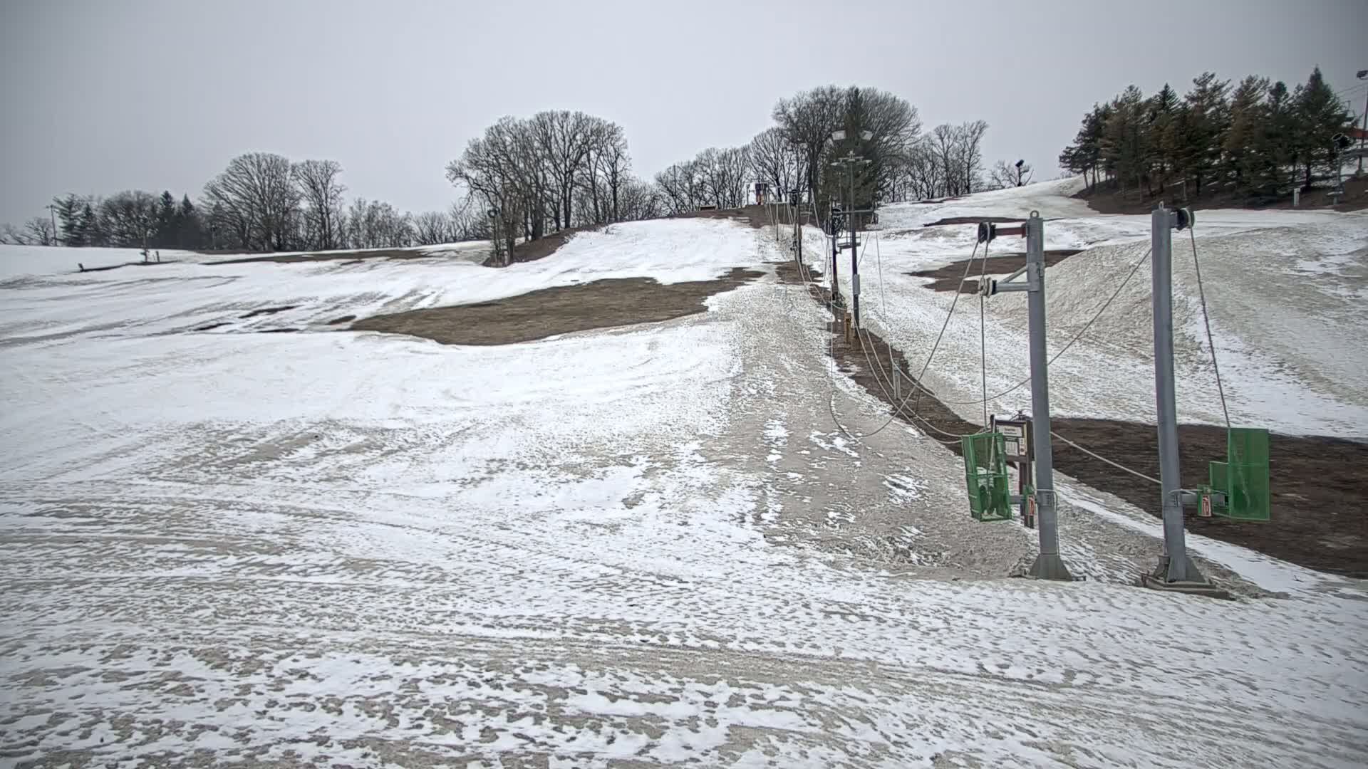 A snow-covered ski slope with a chairlift under an overcast sky.