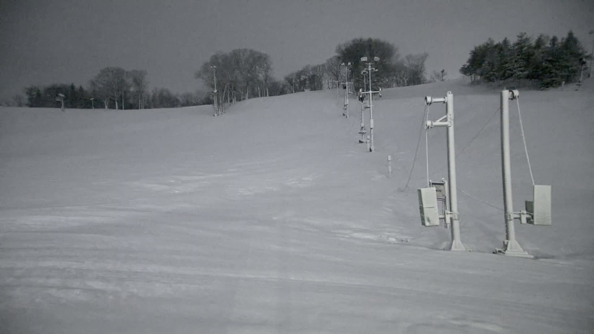 A snow-covered ski slope with a series of empty chairlift supports under an overcast sky.