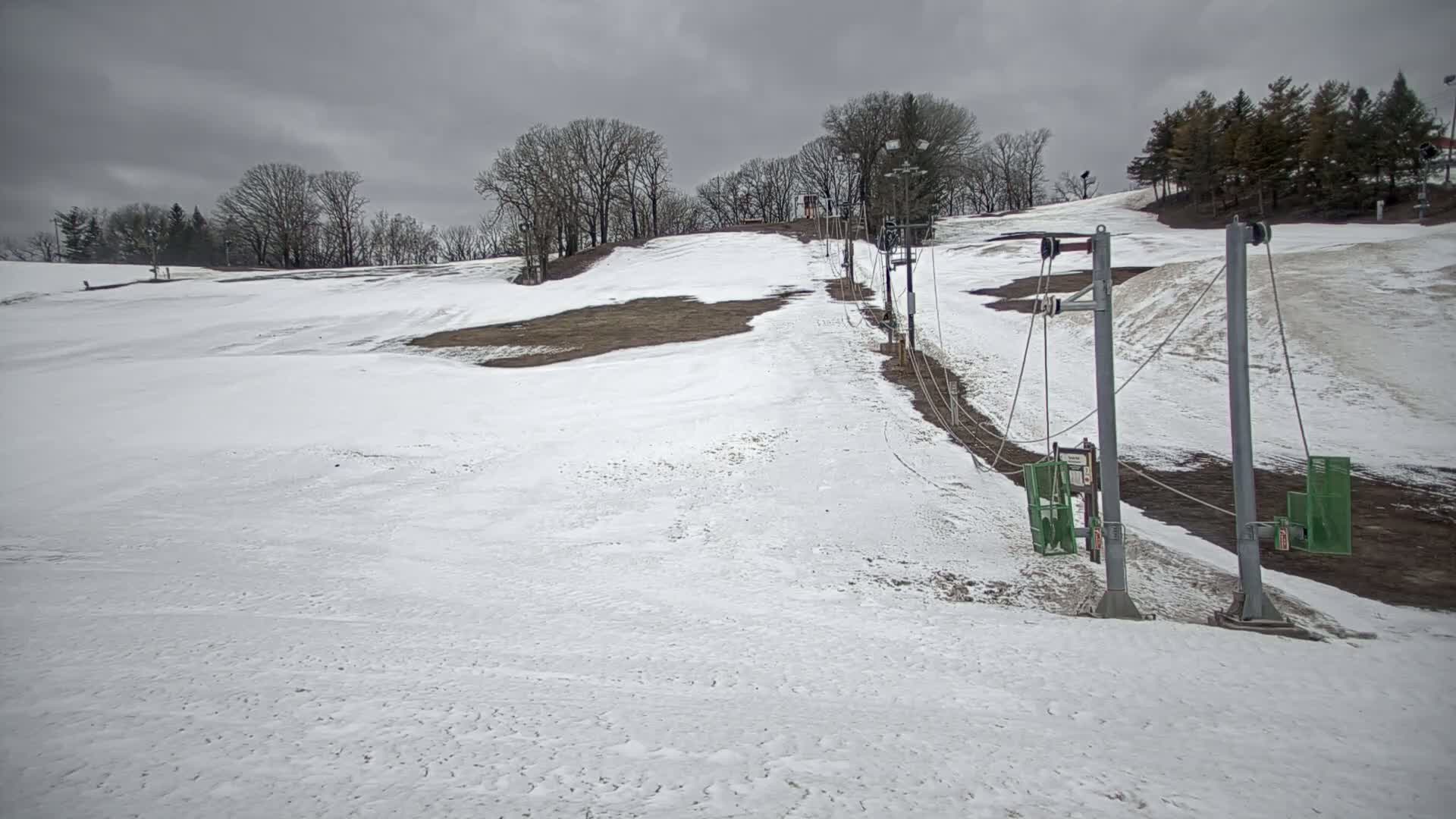 A snow-covered ski slope with a chairlift under an overcast sky.