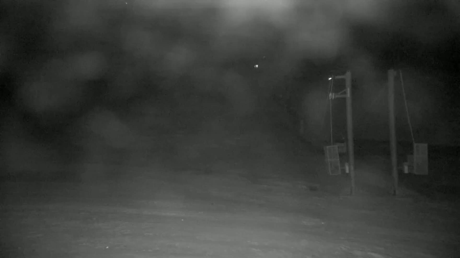 A nighttime, snowy scene shows two tall, thin structures with rectangular boxes attached, under a heavily overcast sky.
