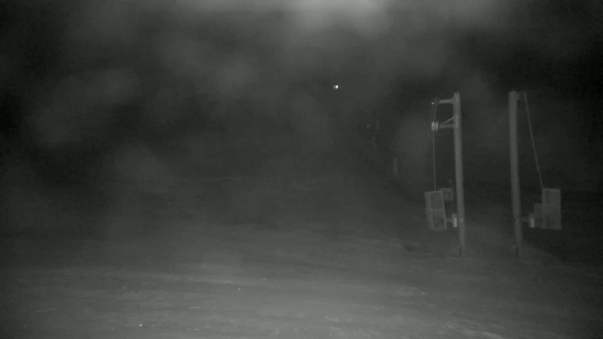 A snowy, nighttime scene shows two tall posts with attached equipment, partially obscured by blowing snow.