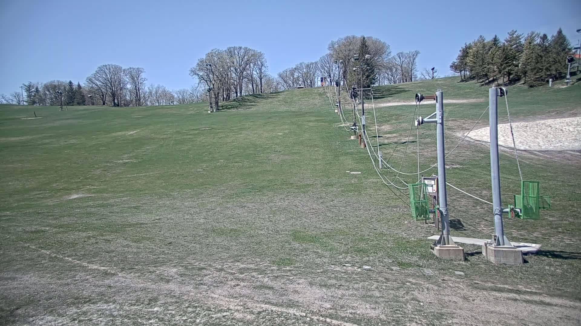 A grassy hill with a ski lift extends from the bottom to the top under a clear blue sky.