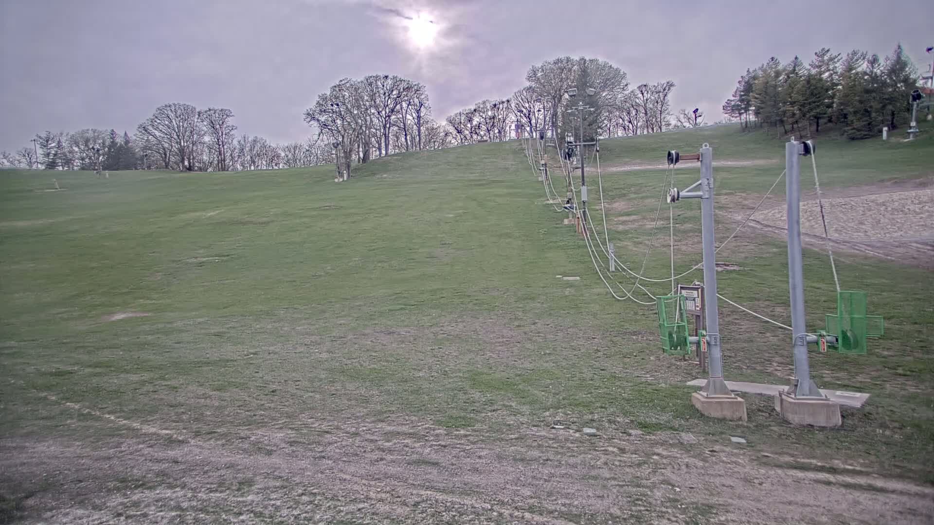 A grassy hill with a dormant ski lift under an overcast sky.