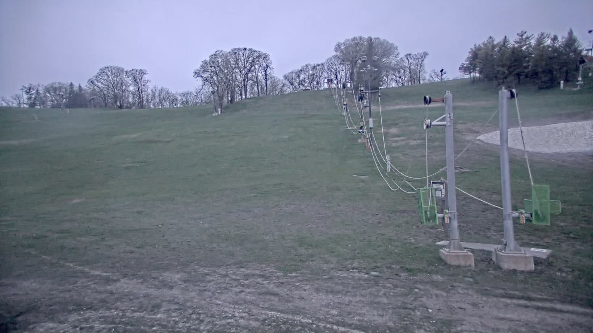 A ski lift extends up a grassy hill under an overcast sky.
