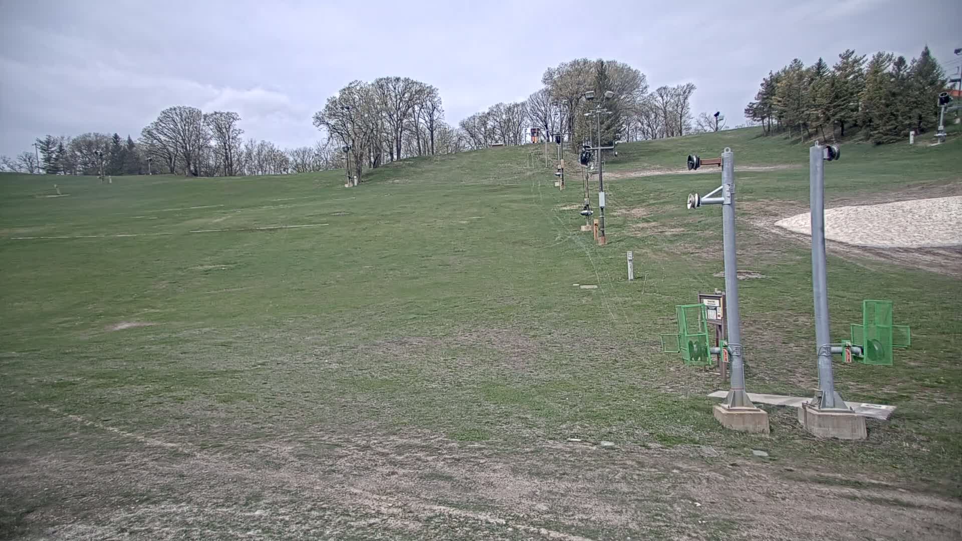 A grassy ski slope with a chairlift extending uphill under an overcast sky.