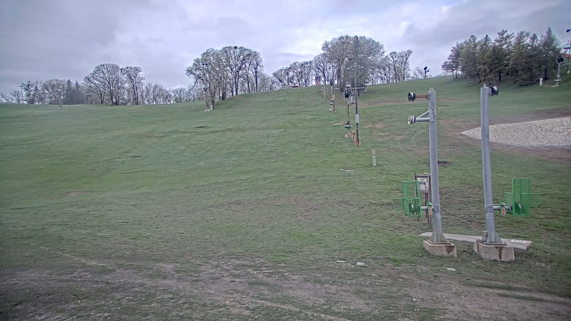 A grassy hill with a ski lift and trees under a cloudy sky.