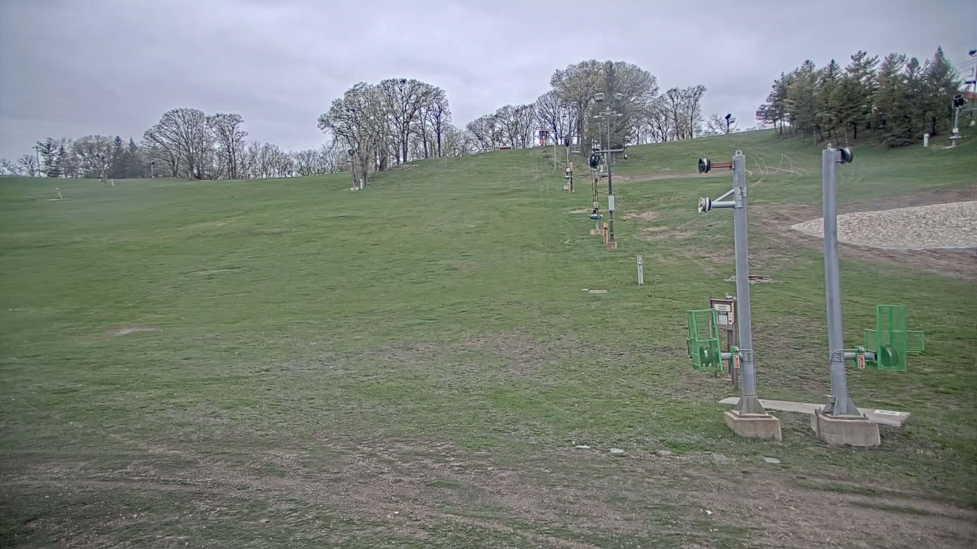 A grassy ski hill with a chairlift under an overcast sky.