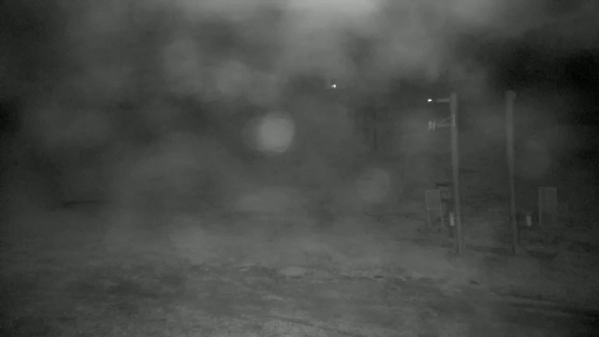 A blurry nighttime scene shows a dimly lit, possibly snowy, area with two upright posts and a hazy atmosphere.