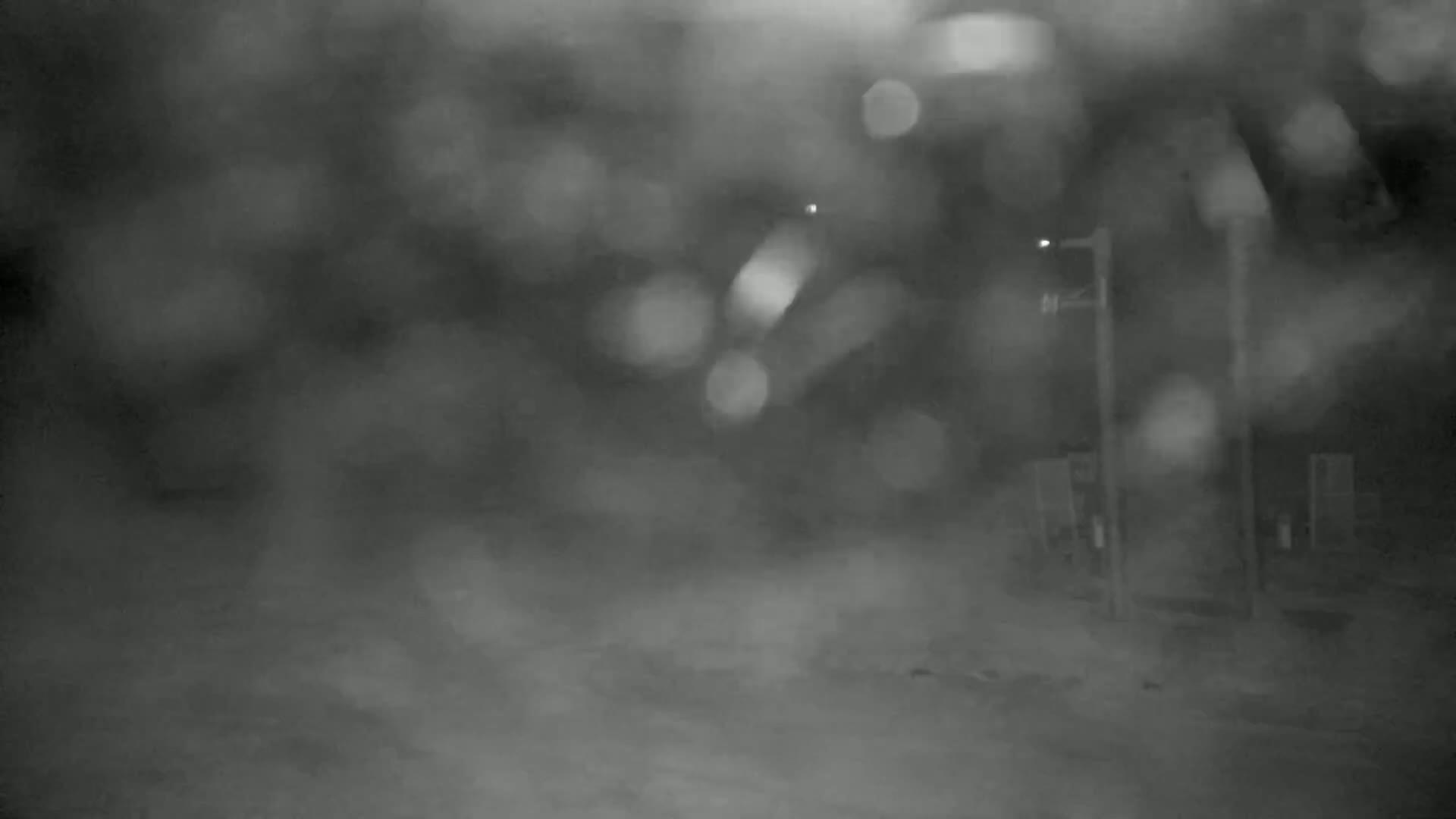 A blurry, nighttime image shows a snow-covered ground and indistinct structures under heavy snowfall.