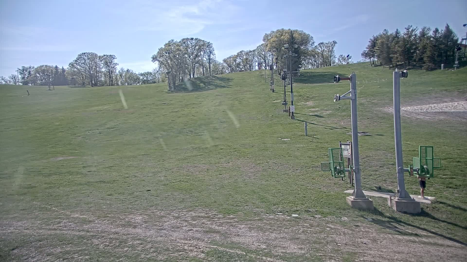 A grassy ski slope with a chairlift, under a mostly sunny sky.