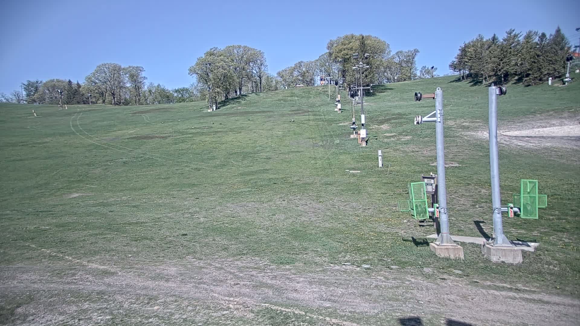 A grassy ski slope with a chairlift and several support poles, under a clear blue sky.