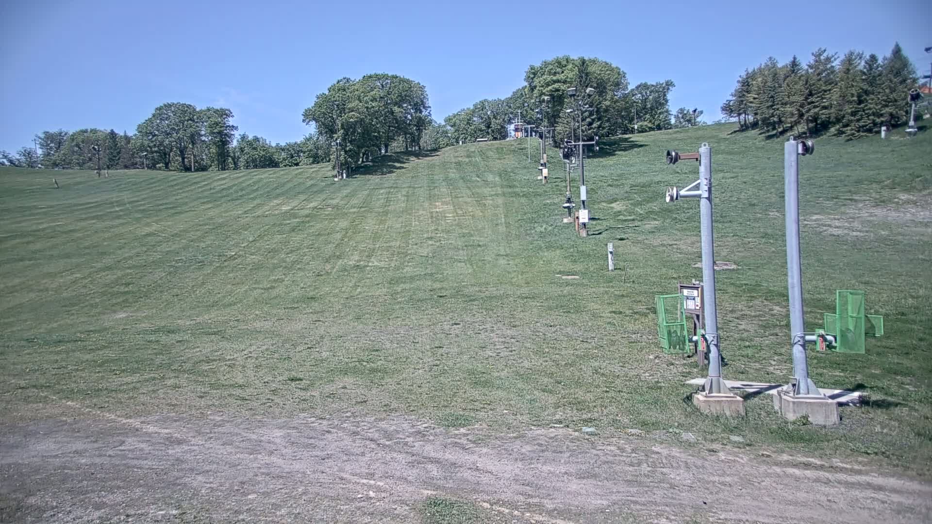 A grassy ski slope with several inactive chairlift poles is visible under a clear blue sky.