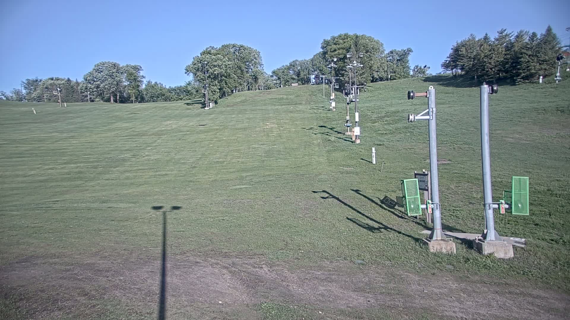 A grassy hill with several ski lift towers is visible under a clear blue sky.