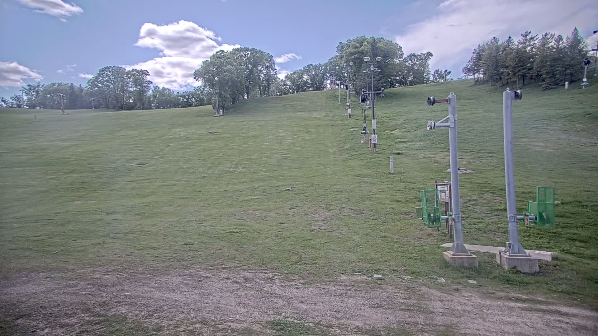A grassy ski slope with a few ski lift poles is visible under a partly cloudy sky.