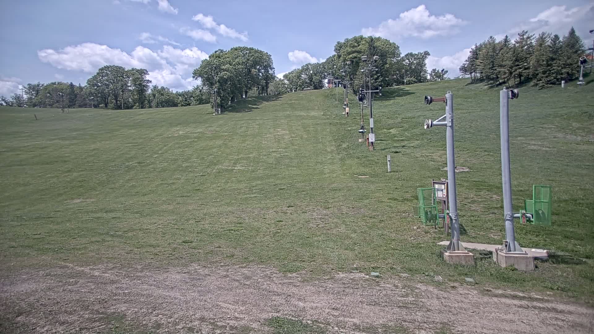 A grassy hill with a ski lift infrastructure is visible under a partly cloudy sky.