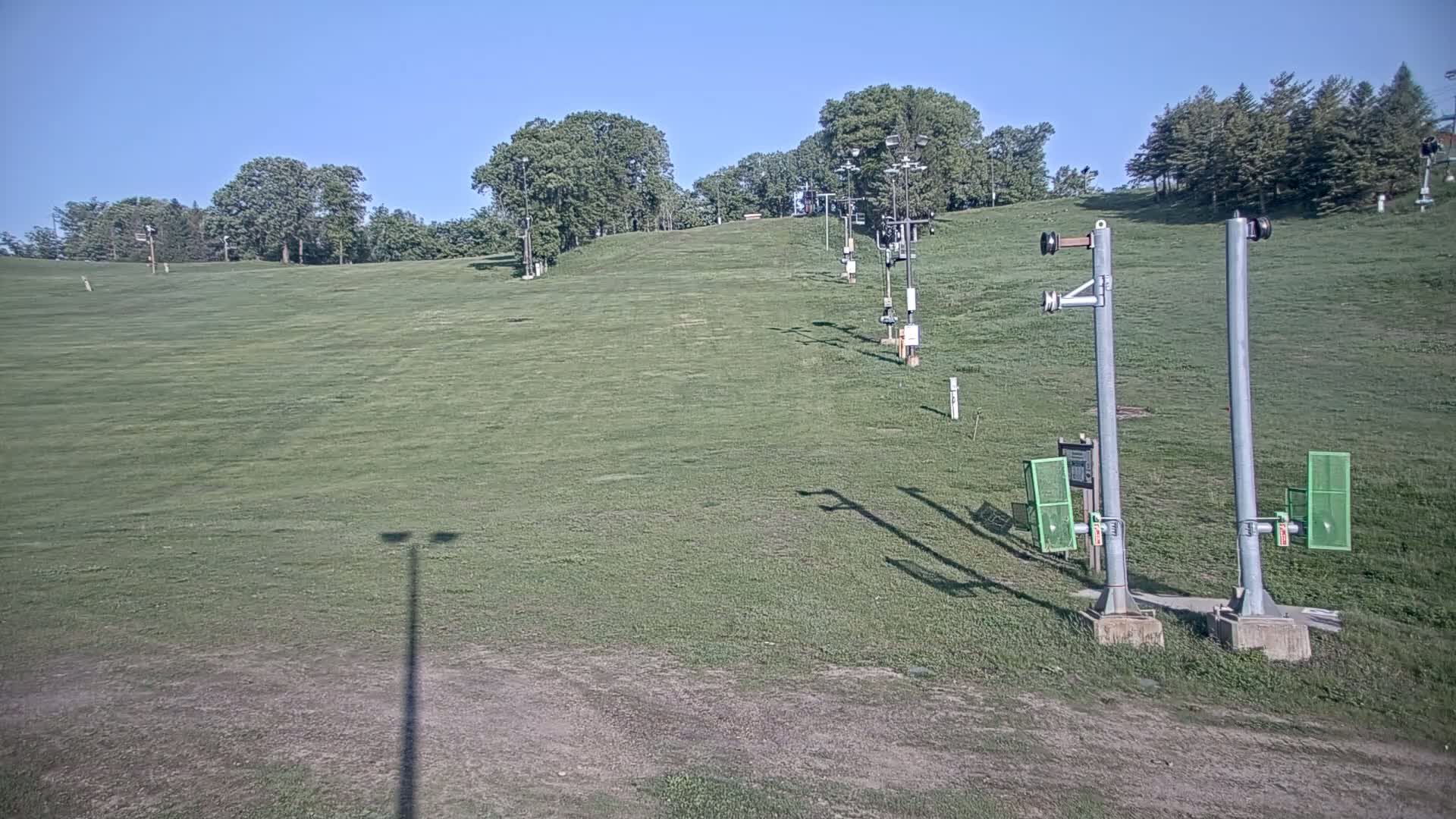 A grassy ski slope with a chairlift and trees under a clear blue sky.