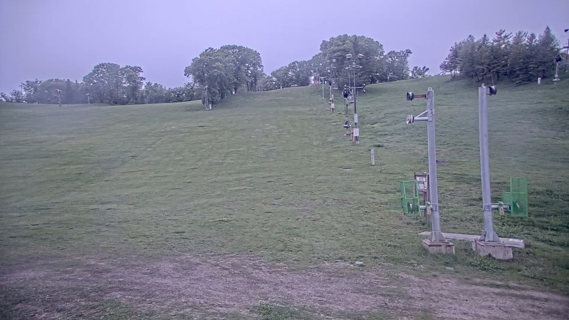 A grassy hill with a ski lift and trees in the background under an overcast sky.