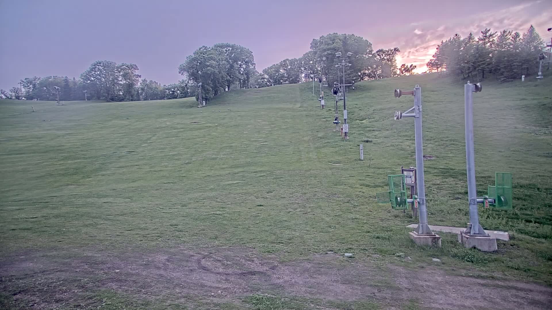 A grassy ski slope with a chairlift and trees in the background under a twilight sky.
