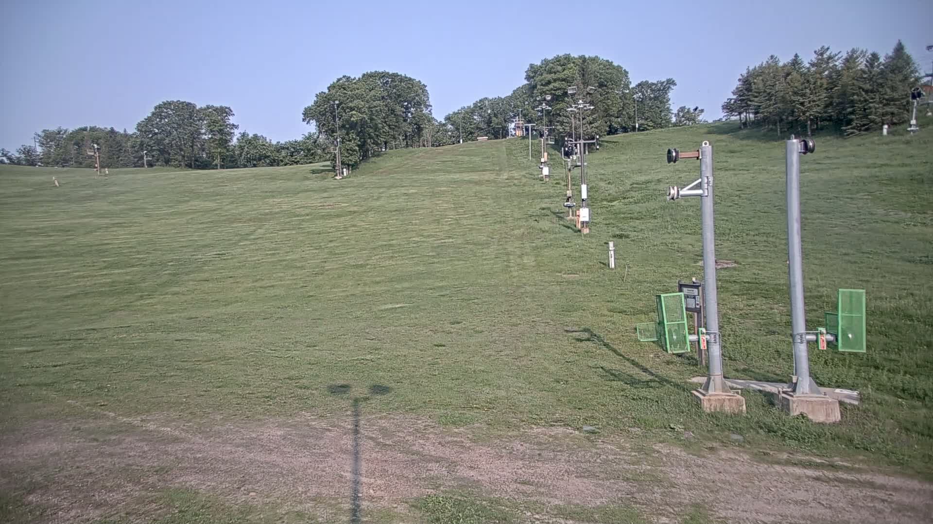 A grassy hill with a ski lift in the background on a clear, sunny day.
