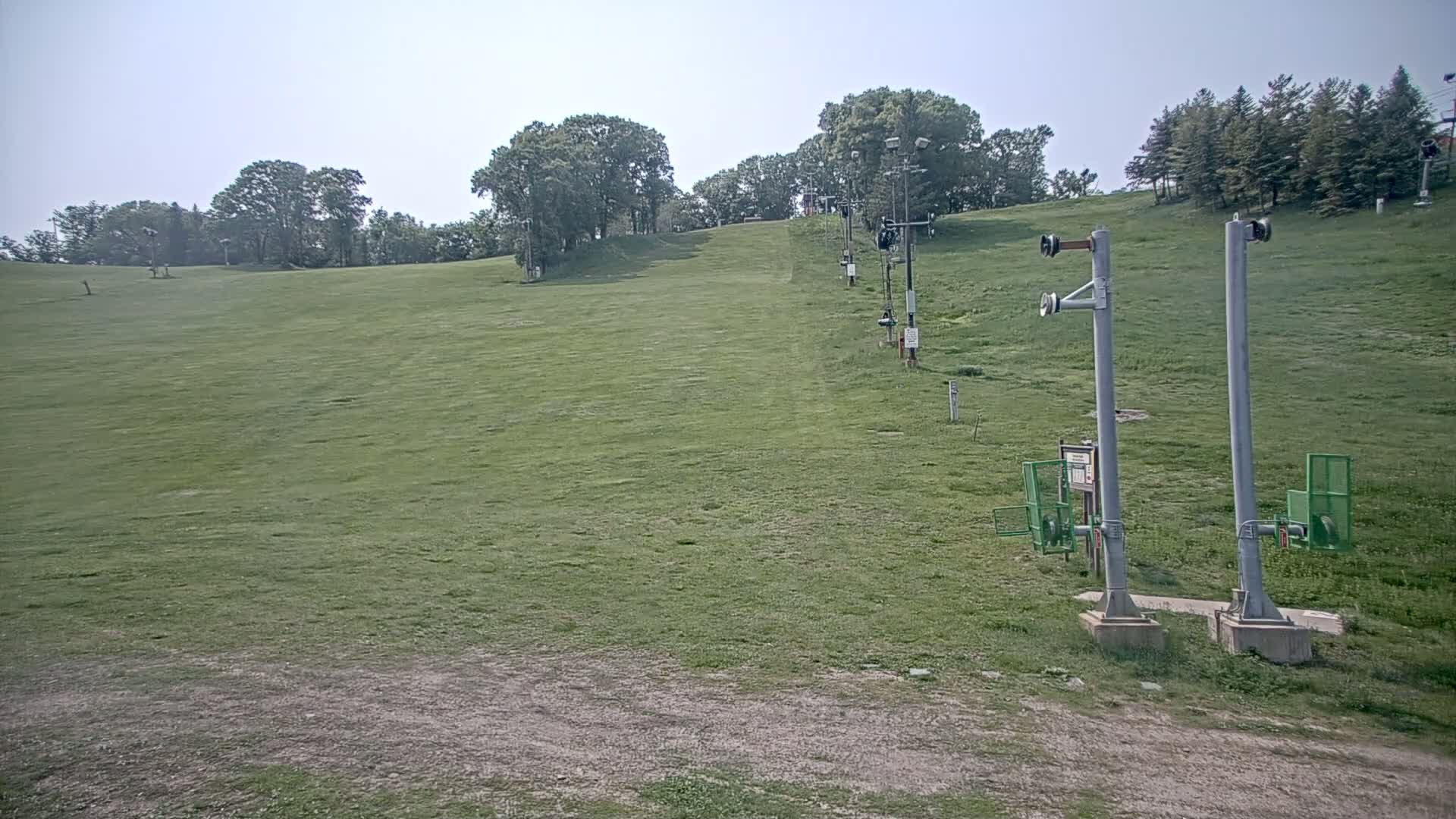 A grassy ski slope with several inactive chairlifts is visible under a clear sky.