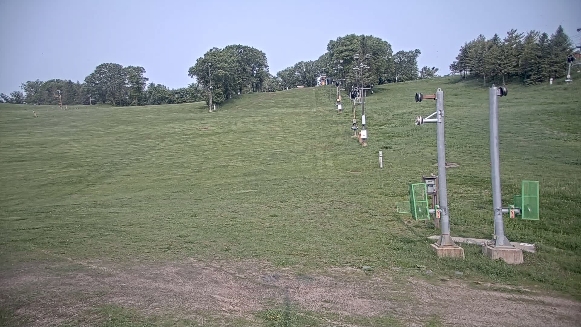 A grassy ski slope with a chairlift in the background under a clear sky.