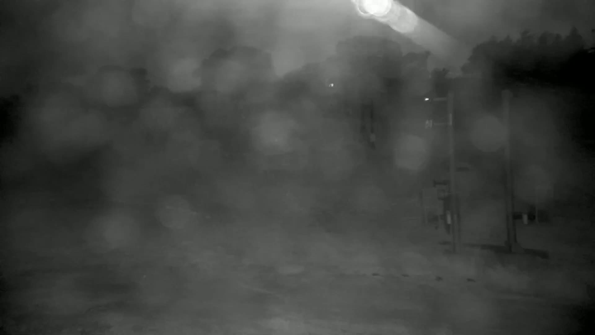 A blurry, nighttime scene shows indistinct shapes and structures in heavy rain or mist.