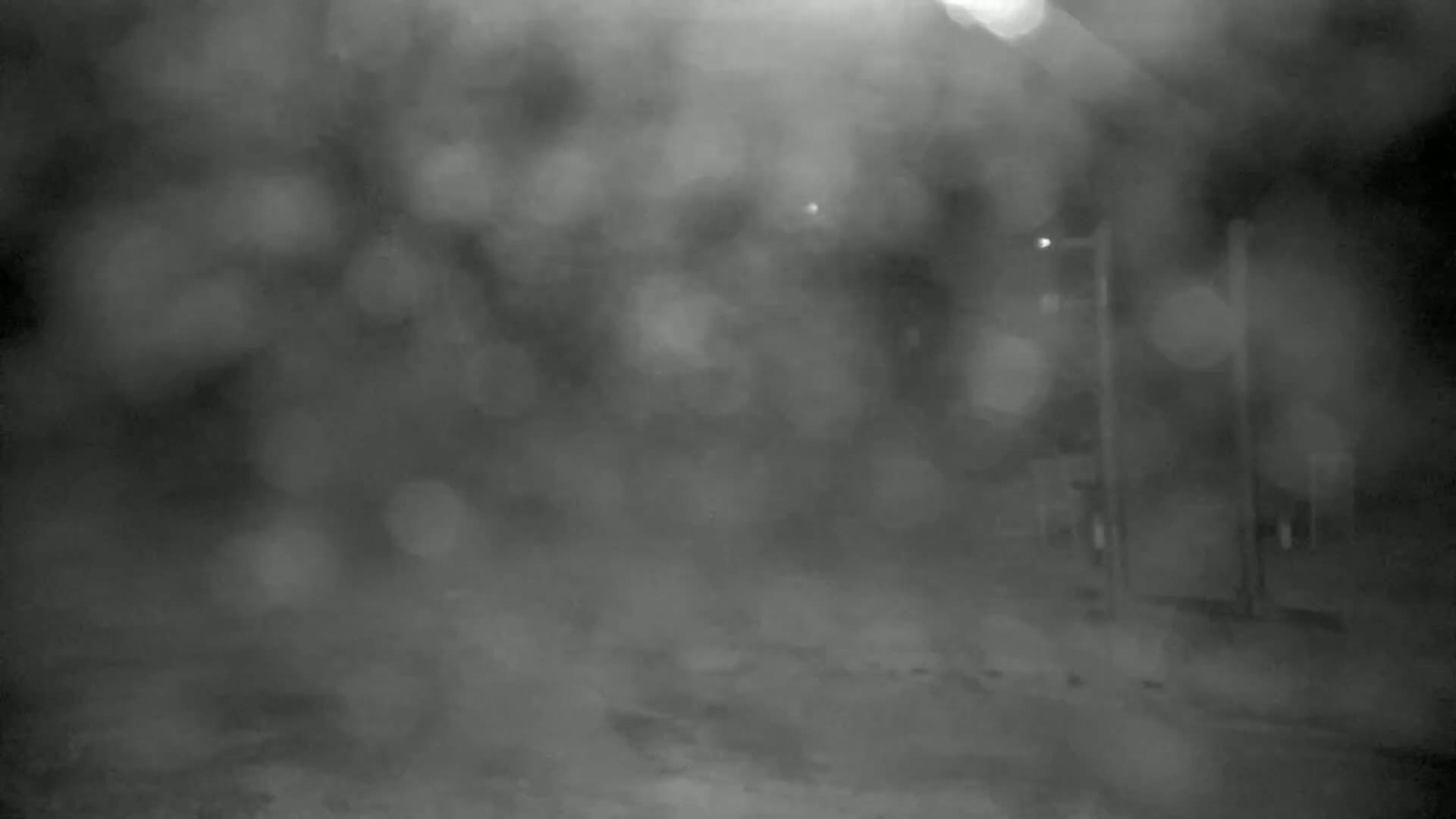 A blurry, nighttime image shows indistinct shapes and lights through heavy fog or mist.