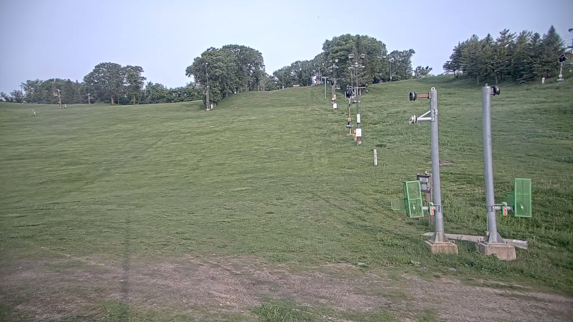A grassy hill with a ski lift infrastructure visible, under a clear sky.