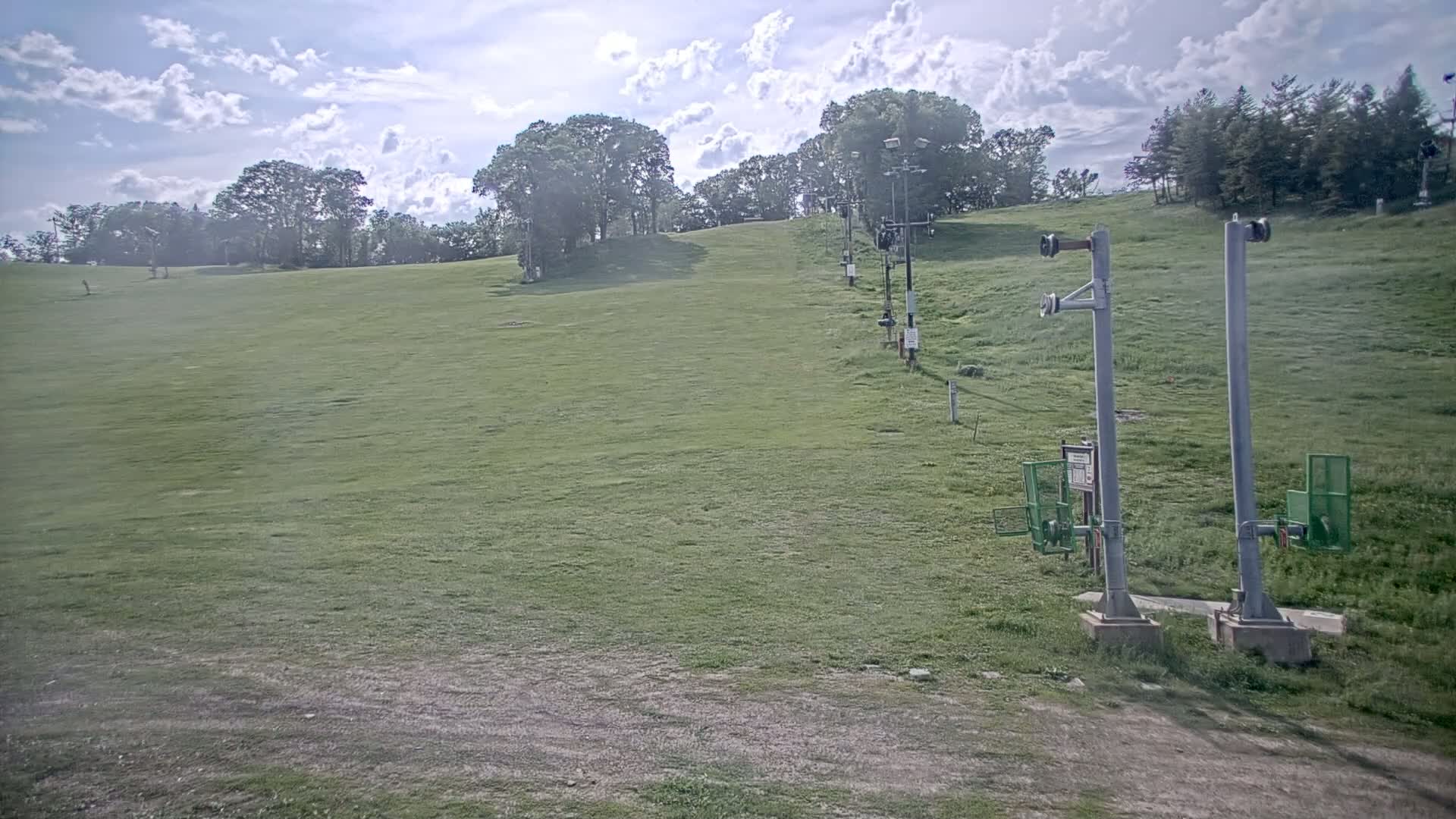 A grassy hillside with a chairlift and trees under a partly cloudy sky.