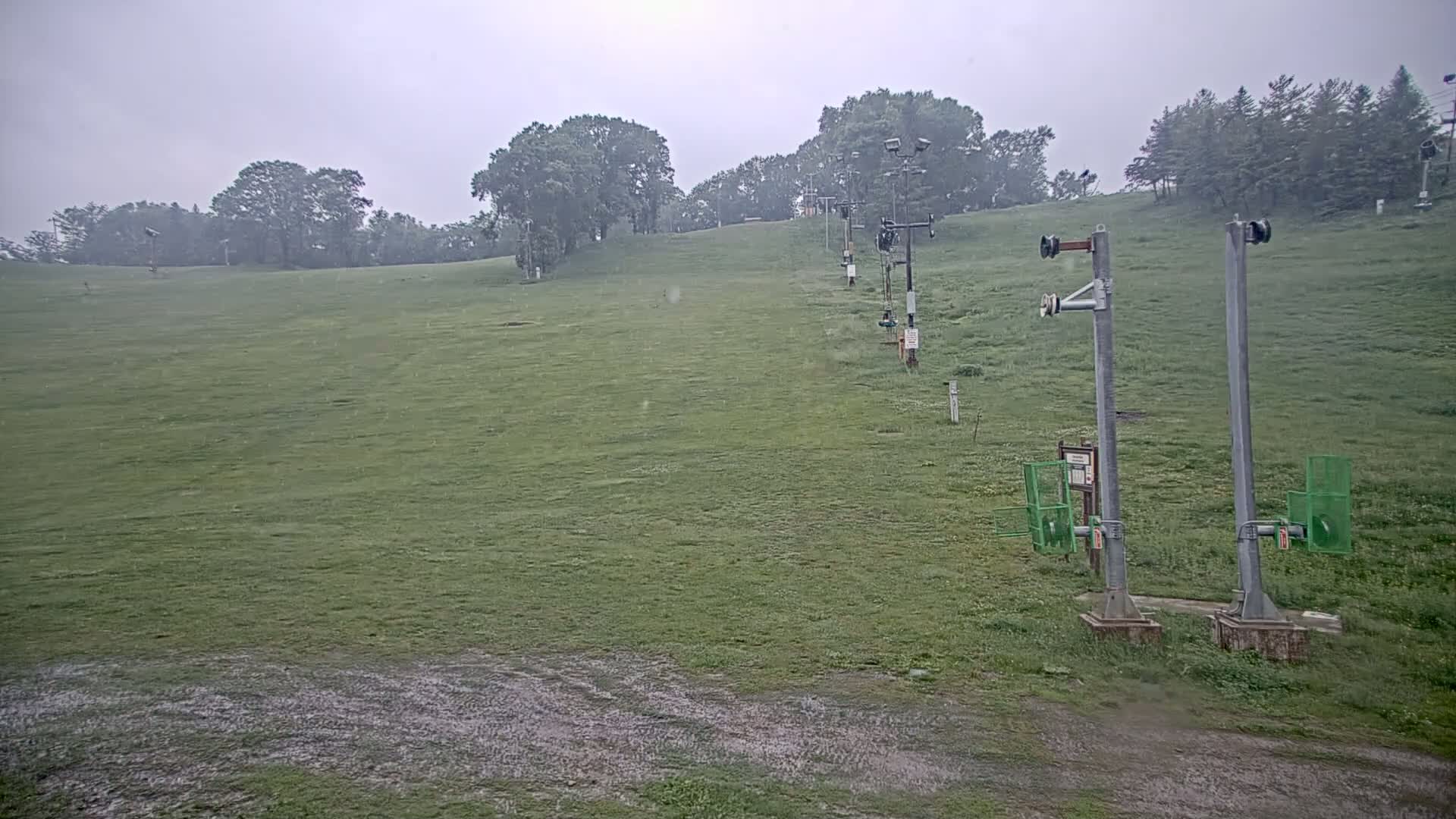 A grassy hill with a ski lift in the rain.