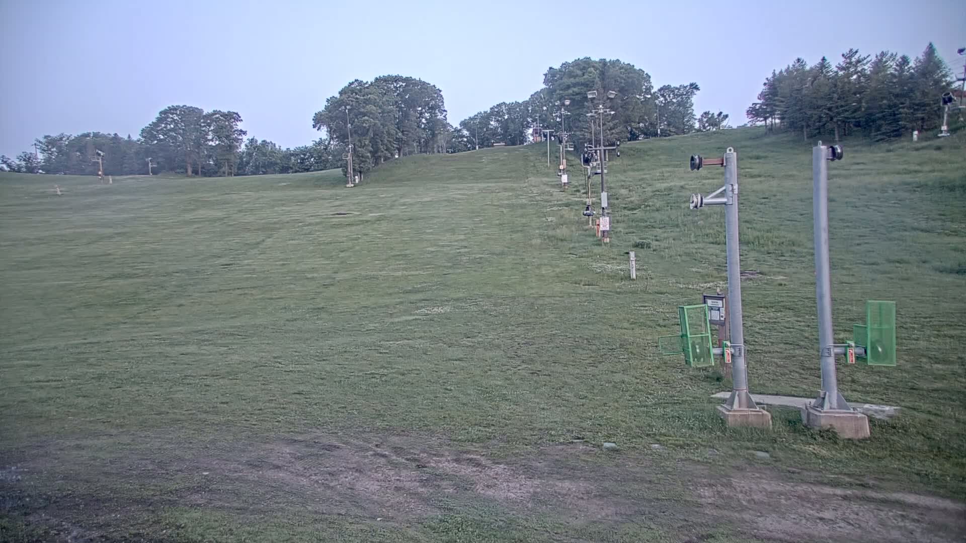 A grassy hill with a ski lift in the background under a cloudy sky.