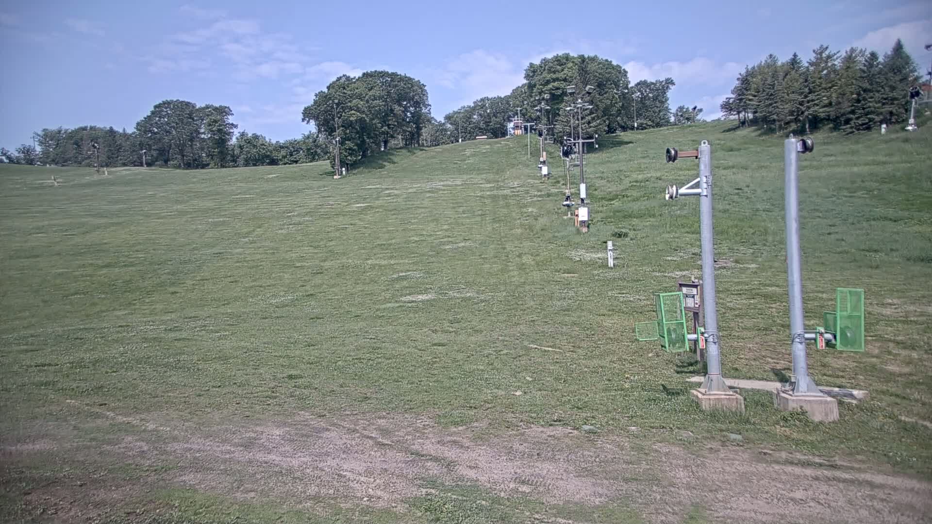 A grassy ski slope with a chairlift and a mostly sunny sky.