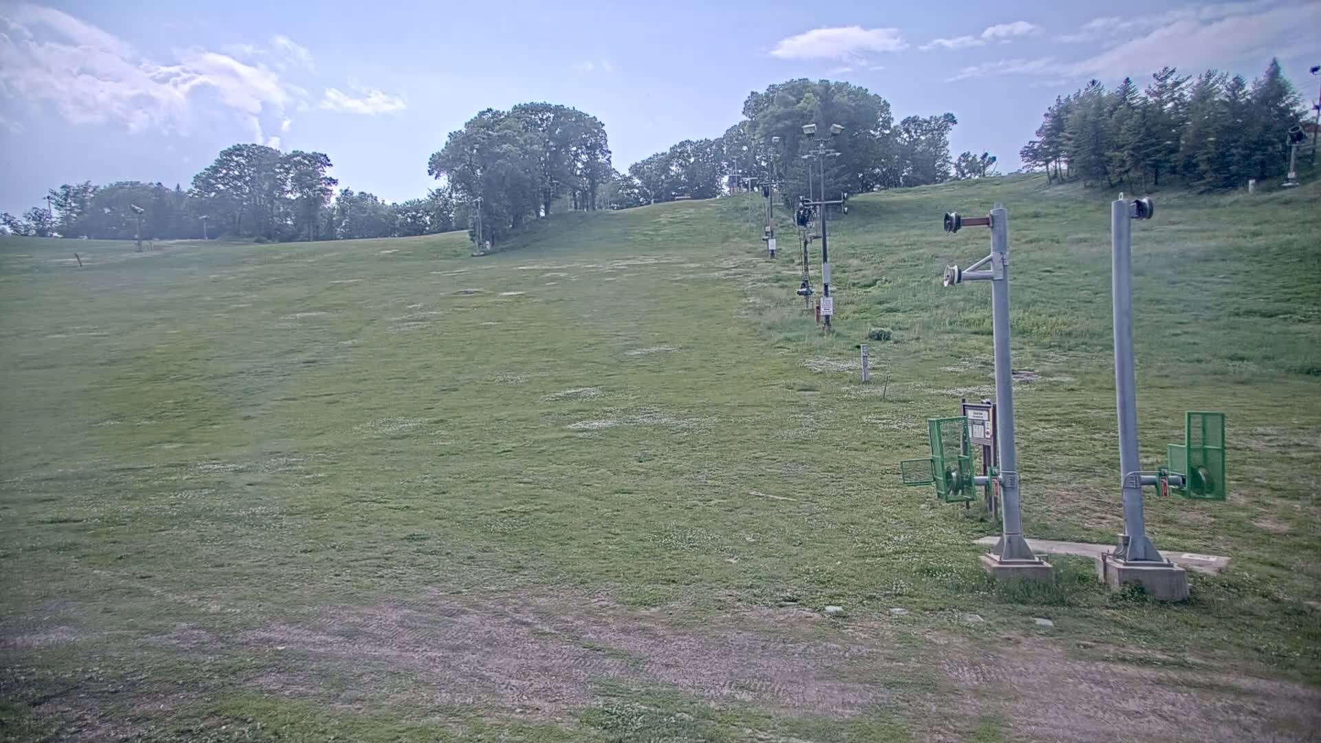 A grassy hill with a chairlift infrastructure under a partly cloudy sky.
