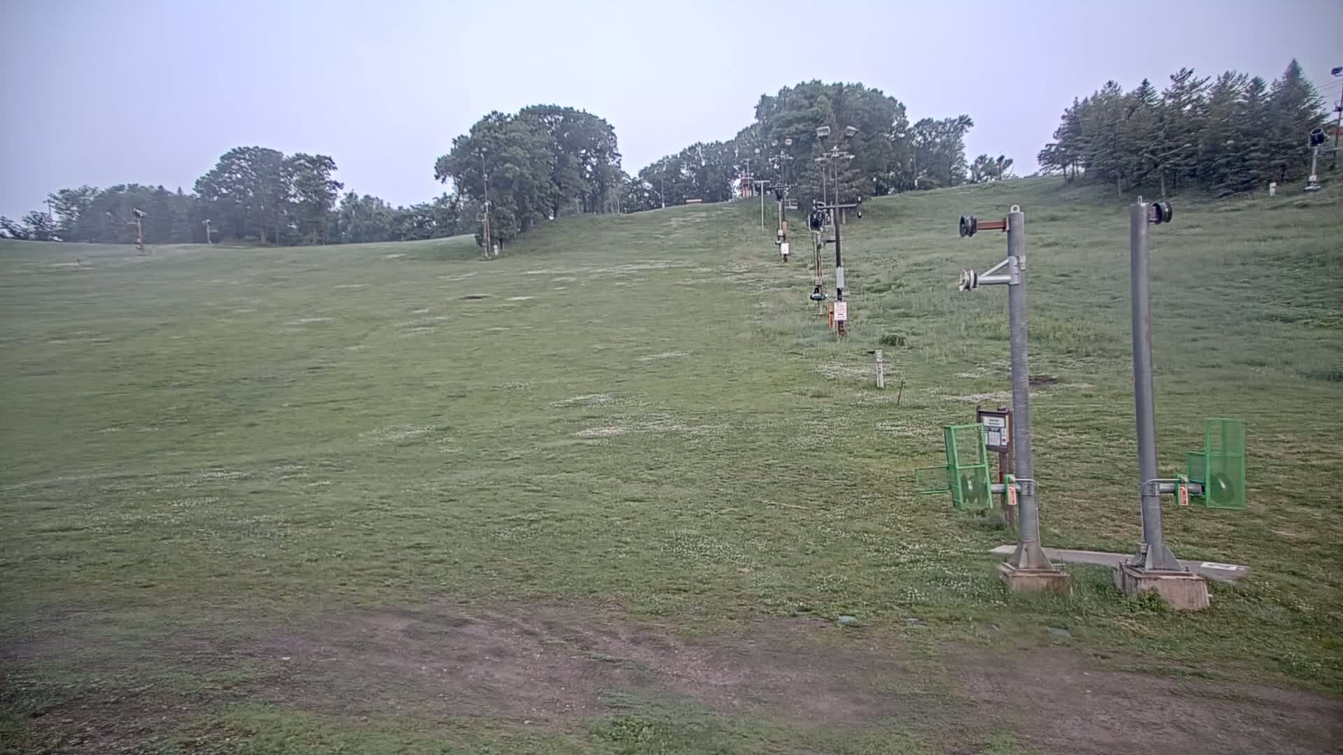 A grassy hill with a ski lift in the background under an overcast sky.