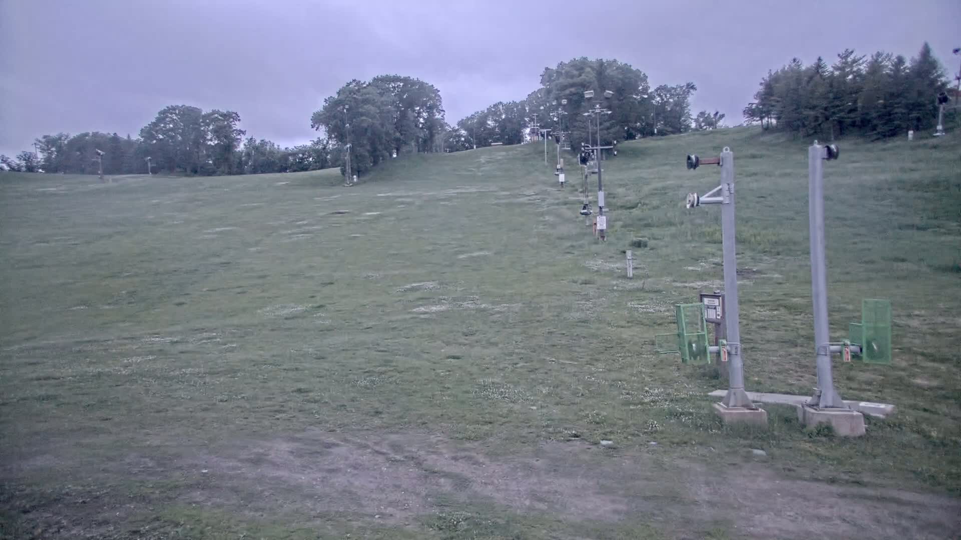 A grassy hill with a chairlift extending upward, under an overcast sky.