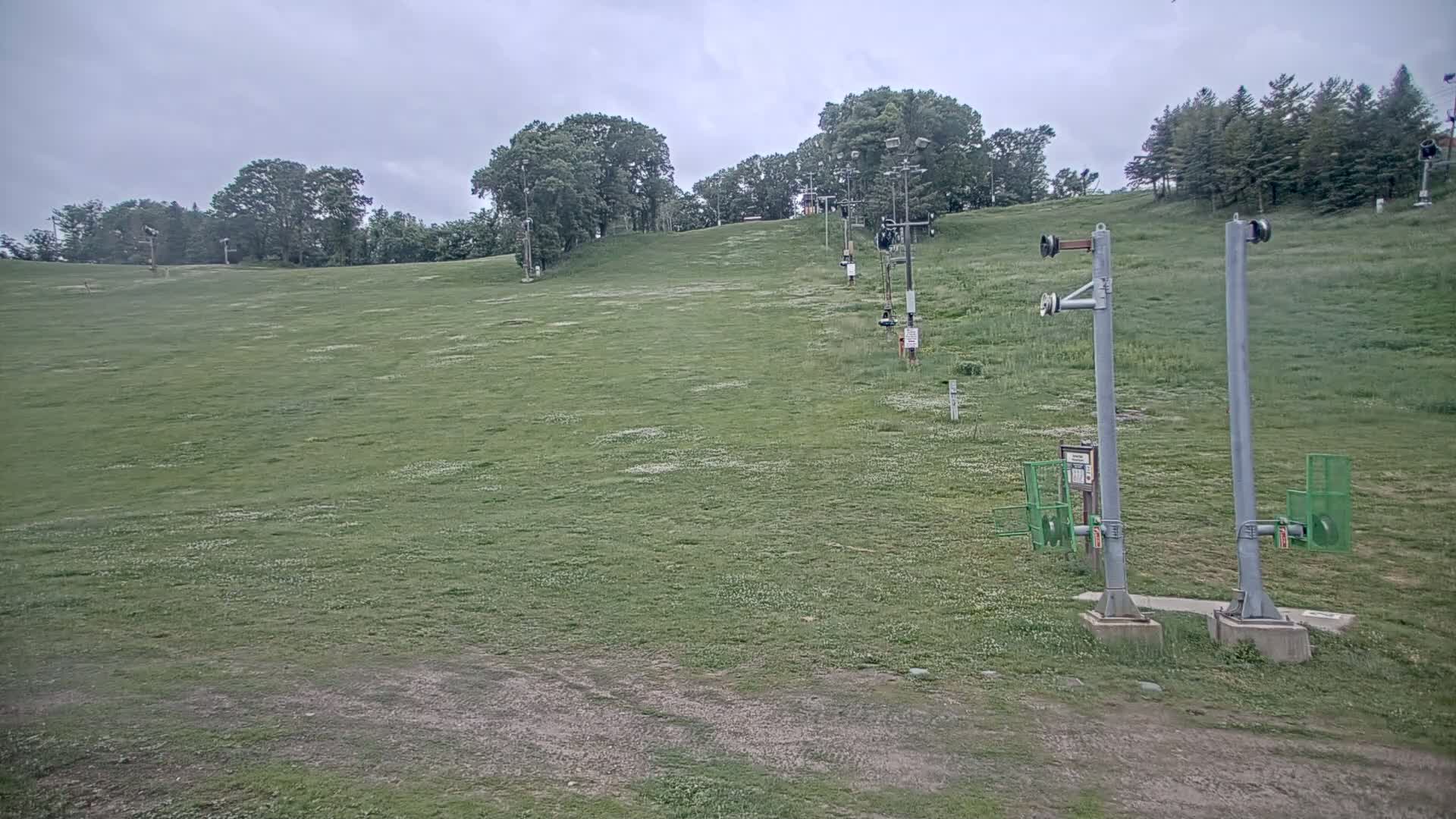 A grassy hillside with a chairlift, under a cloudy sky.