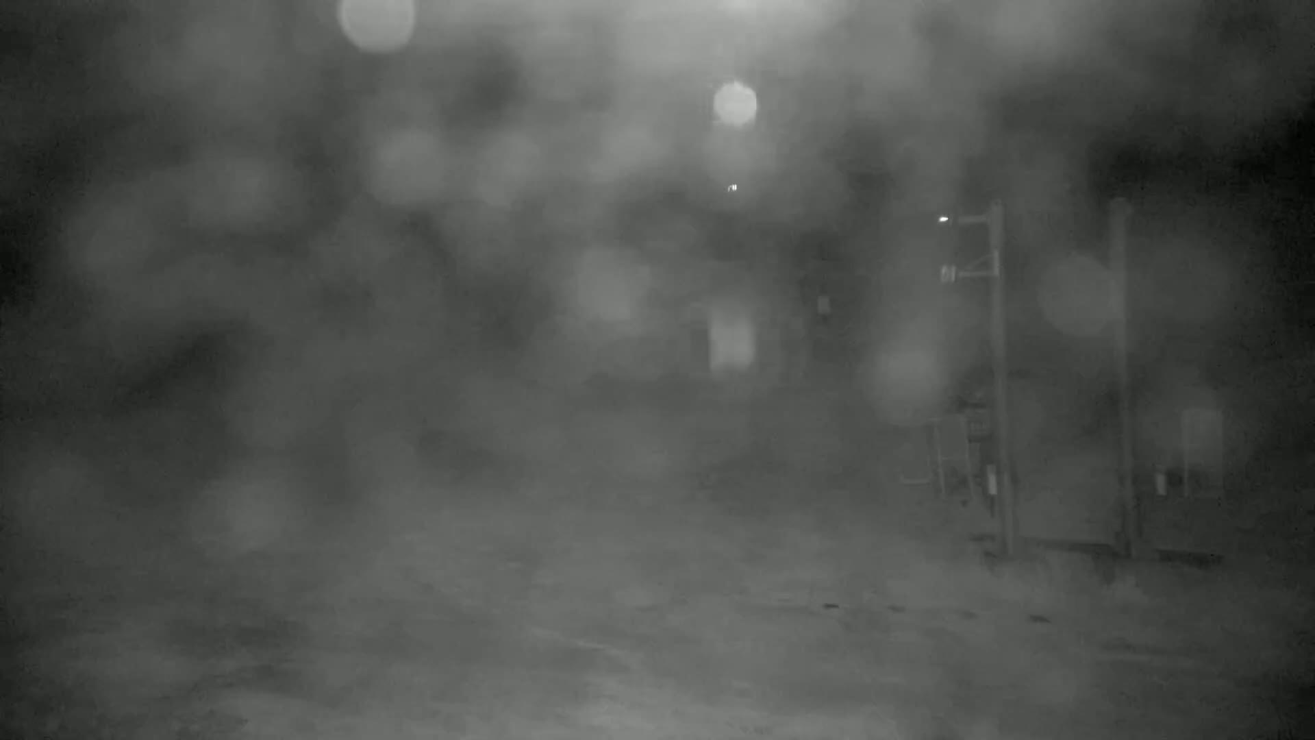 A blurry, nighttime scene of a street with a building and a streetlight in heavy fog or snow.
