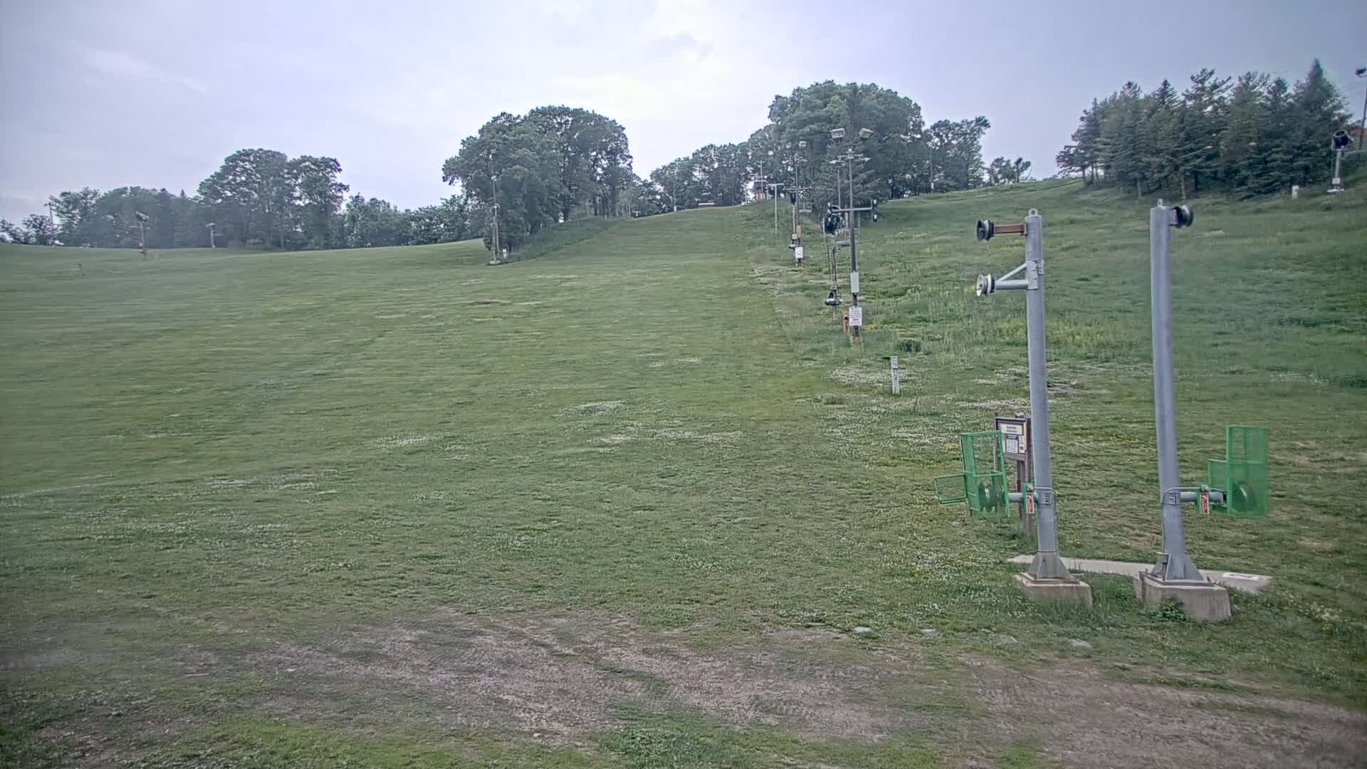 A grassy ski slope with inactive chairlift infrastructure is visible under an overcast sky.