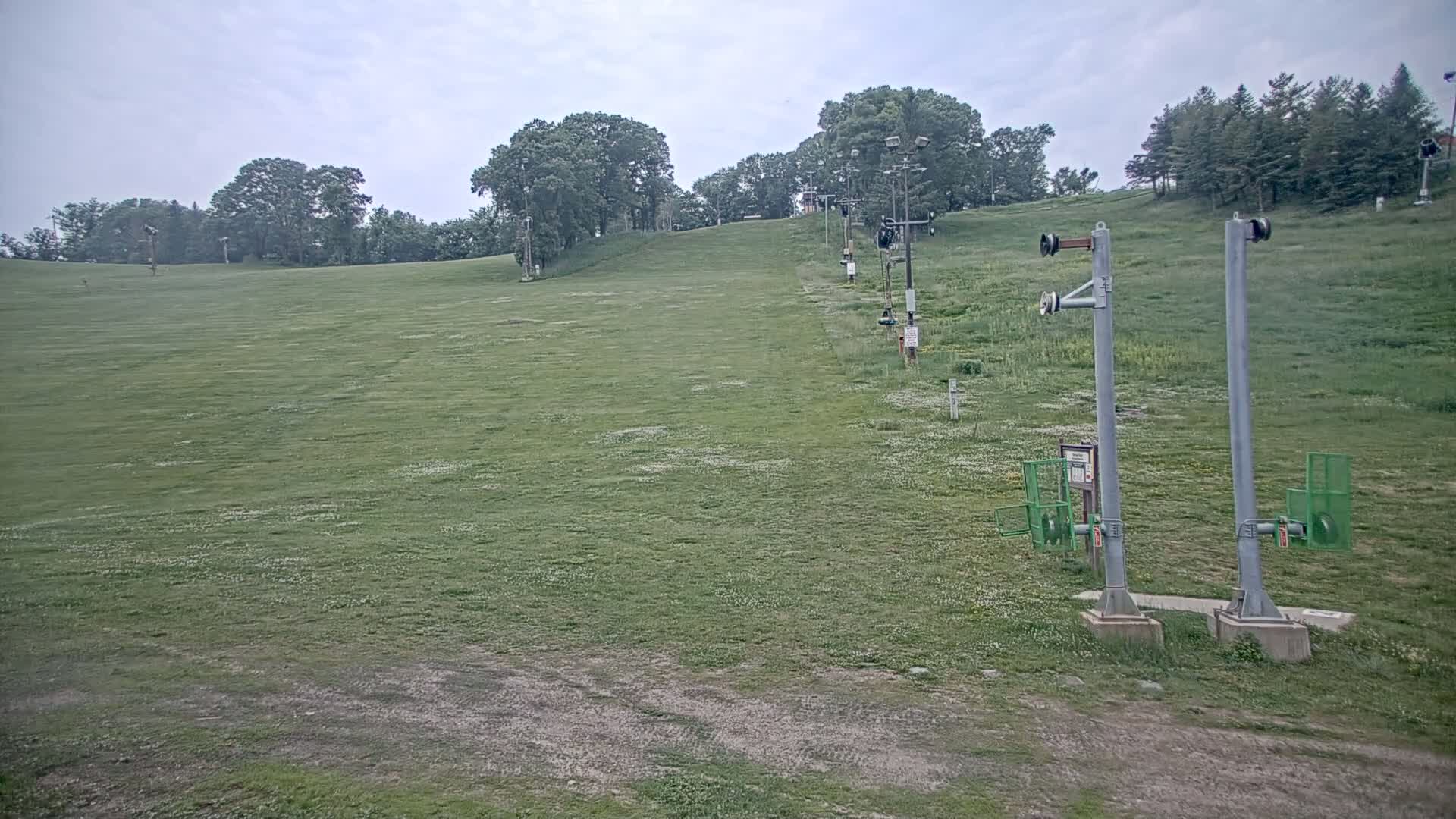 A grassy hill with a ski lift in the background under an overcast sky.