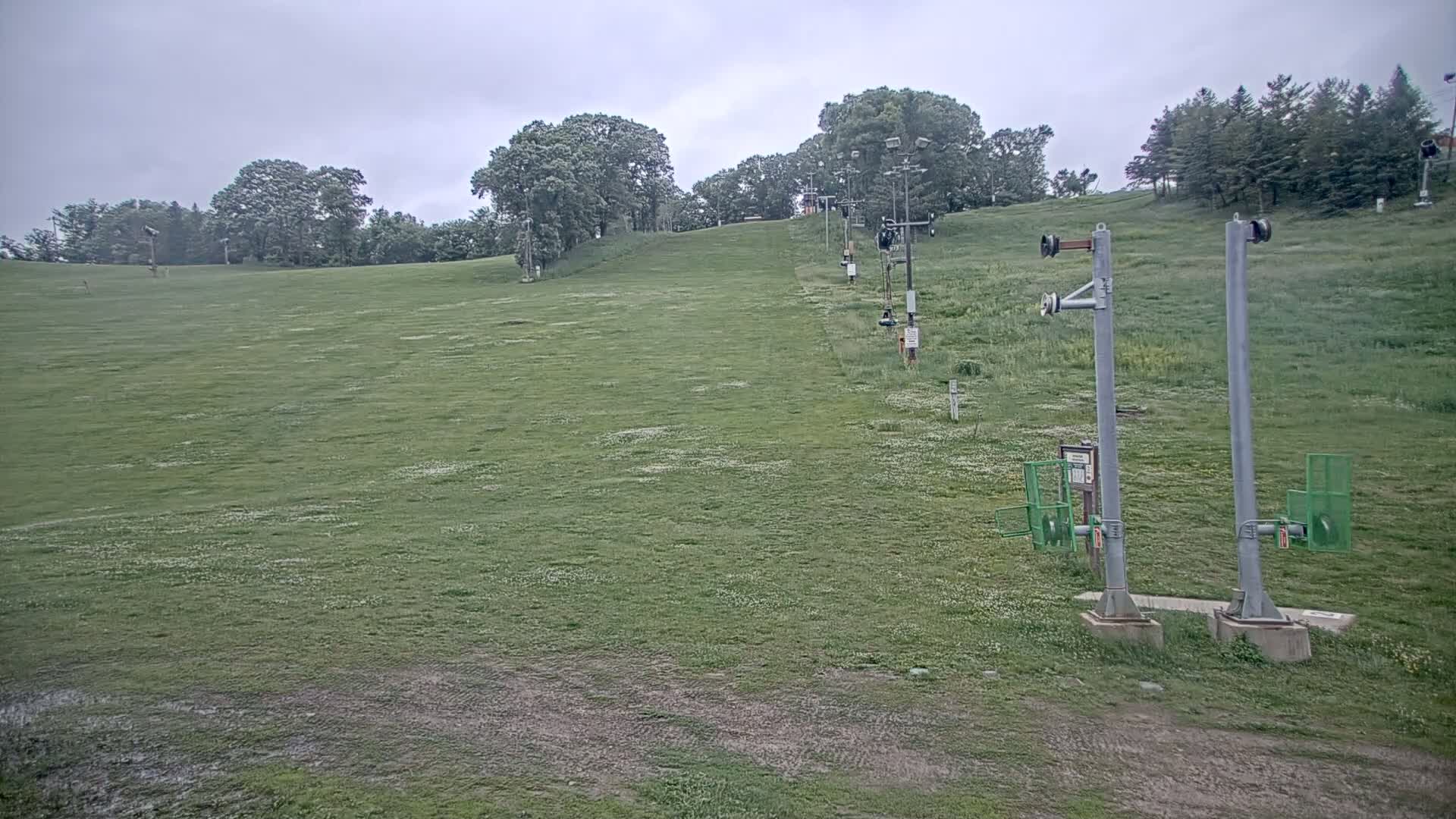A grassy hill with a ski lift visible, under an overcast sky.