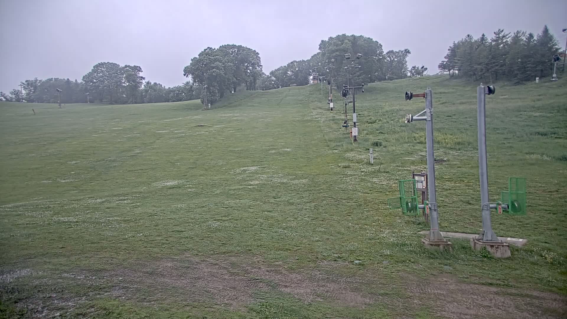 A grassy hill with a ski lift in the background on an overcast day.