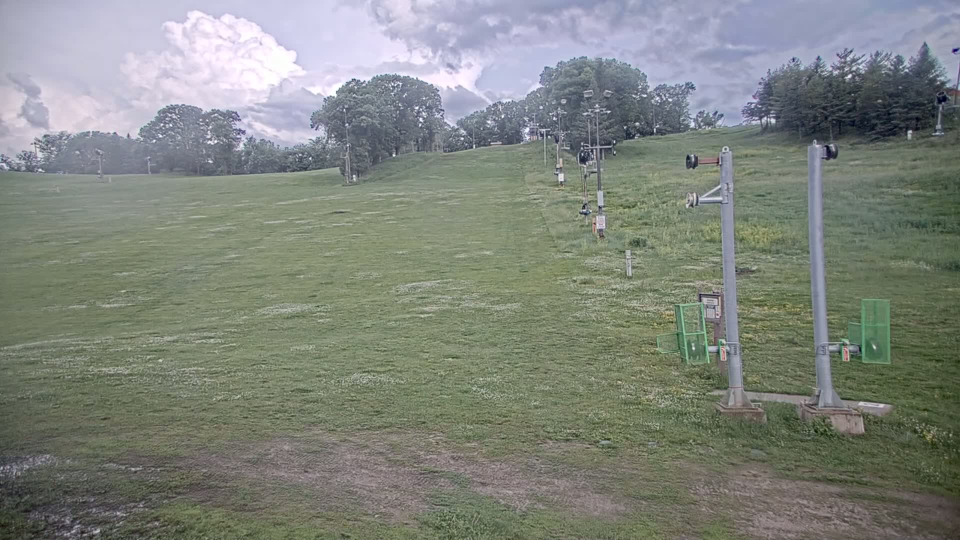 A grassy hill with a chairlift extending upwards, under a cloudy sky.