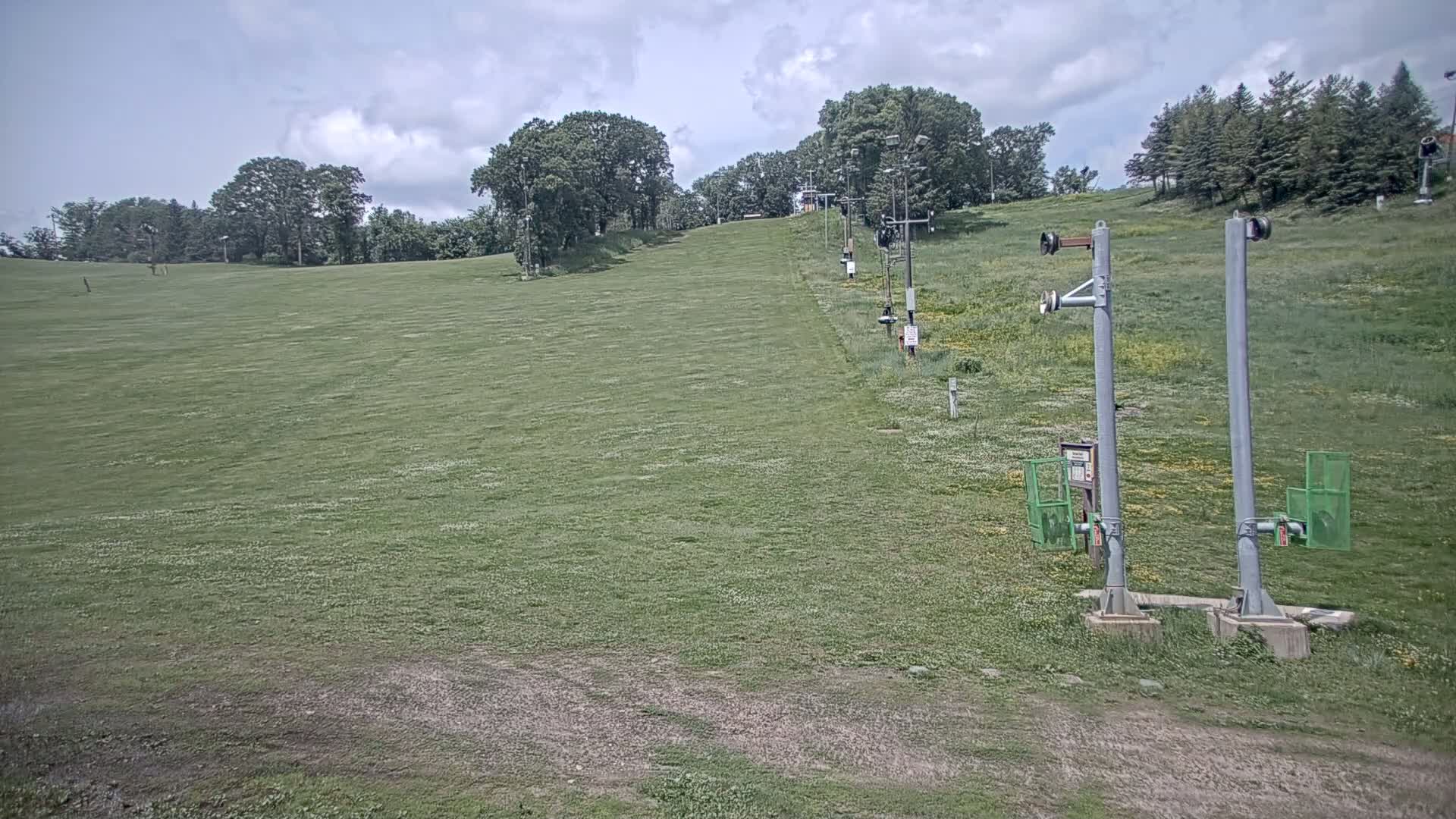 A grassy hill with a chairlift and trees in the background under a partly cloudy sky.