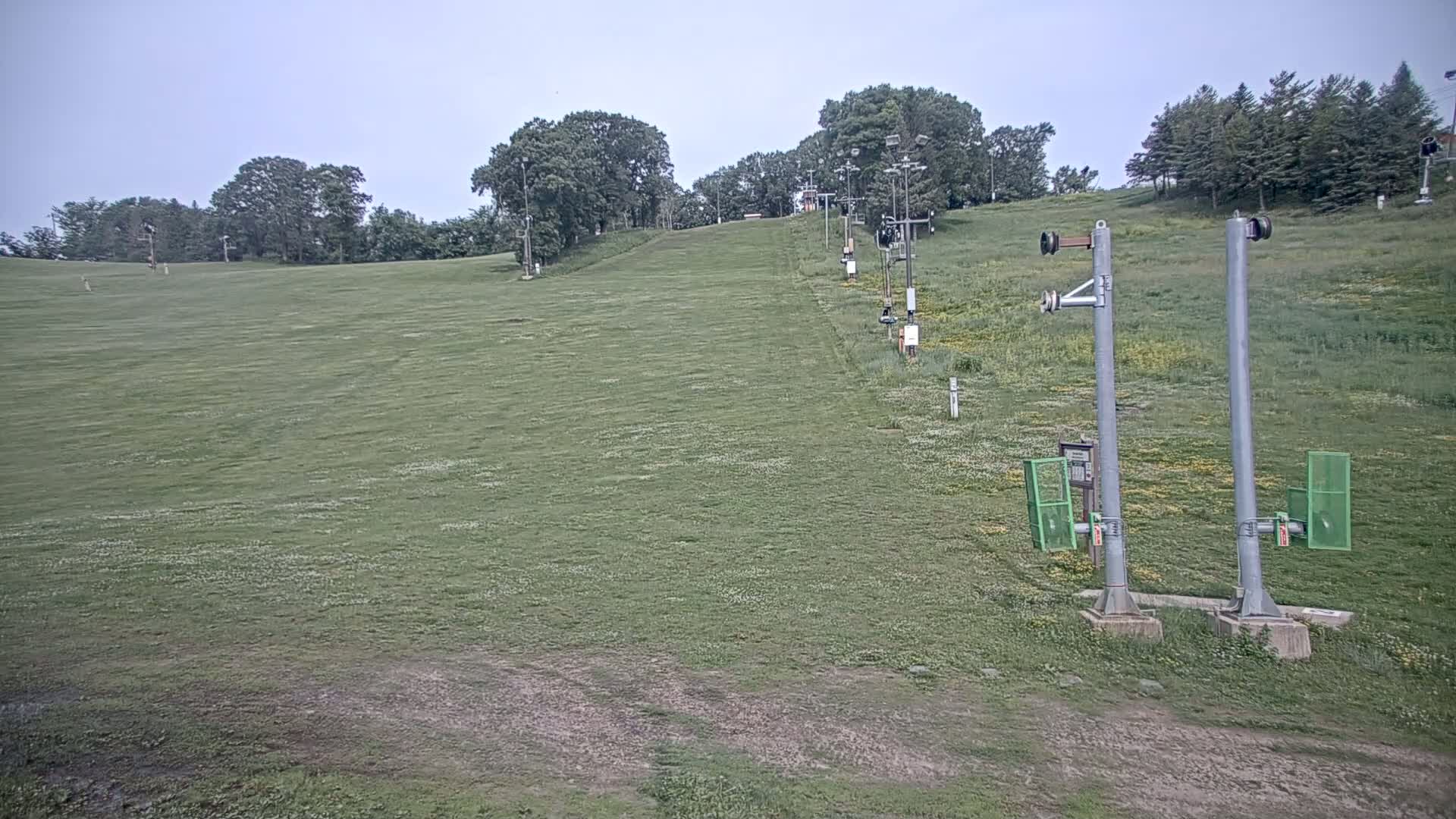 A grassy hill with a chairlift extending uphill under an overcast sky.