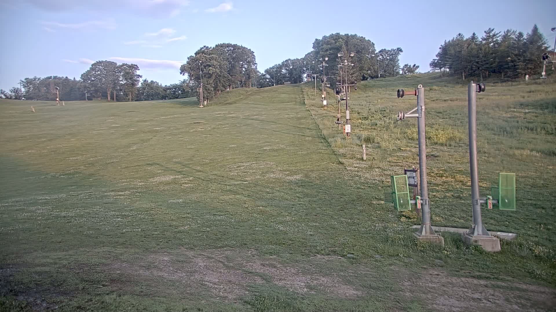A grassy ski slope with a chairlift in the background under a mostly clear sky.