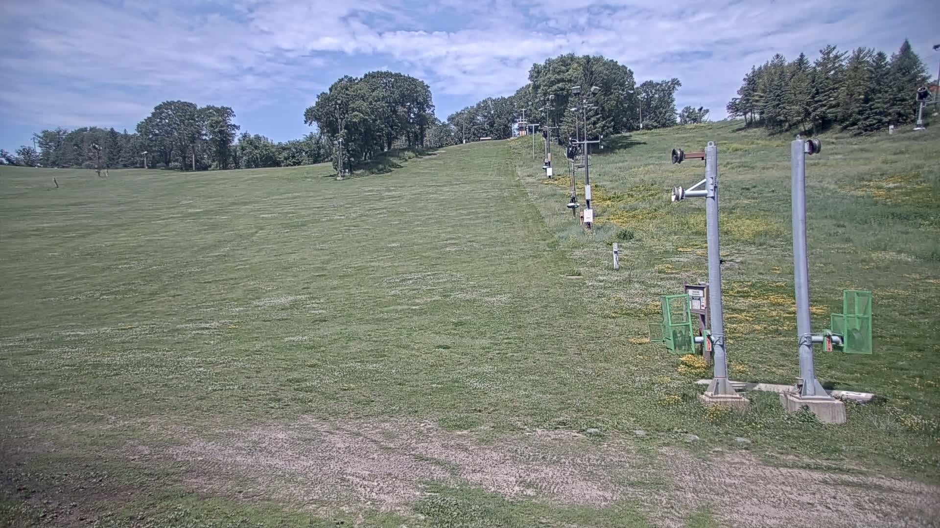 A grassy hillside with a chairlift runs up the hill under a partly cloudy sky.